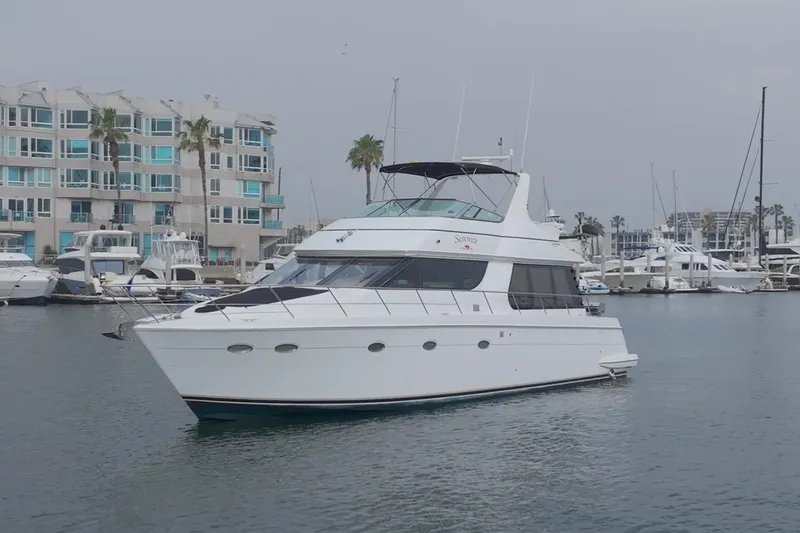 The Image of 1999 Carver 53 Voyager yacht docked in a marina with modern buildings in the background. - 0