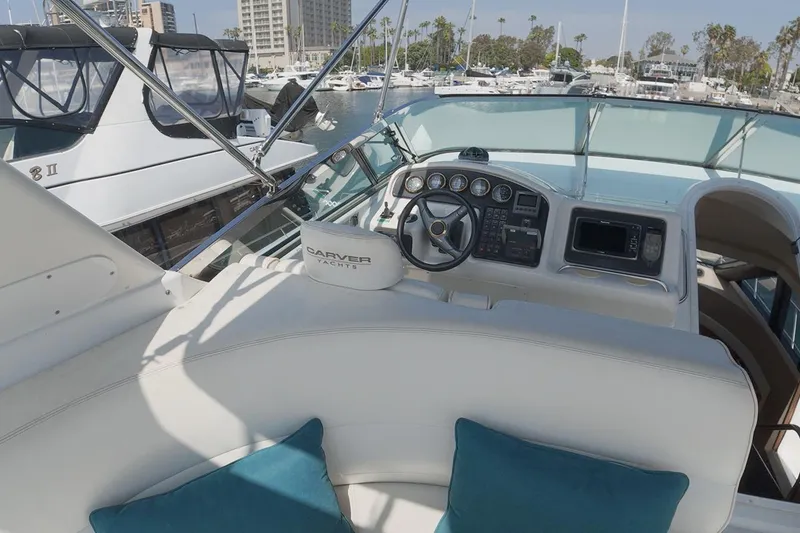Slide: The Image of 1999 Carver 53 Voyager yacht helm with marina view, featuring plush seating and navigation controls. - 18