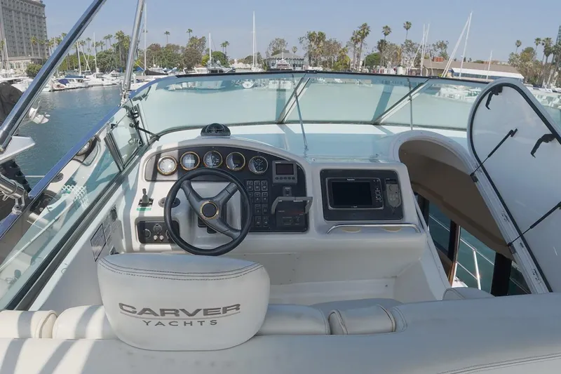 Slide: The Image of 1999 Carver 53 Voyager yacht helm with steering wheel and navigation controls in marina setting. - 19