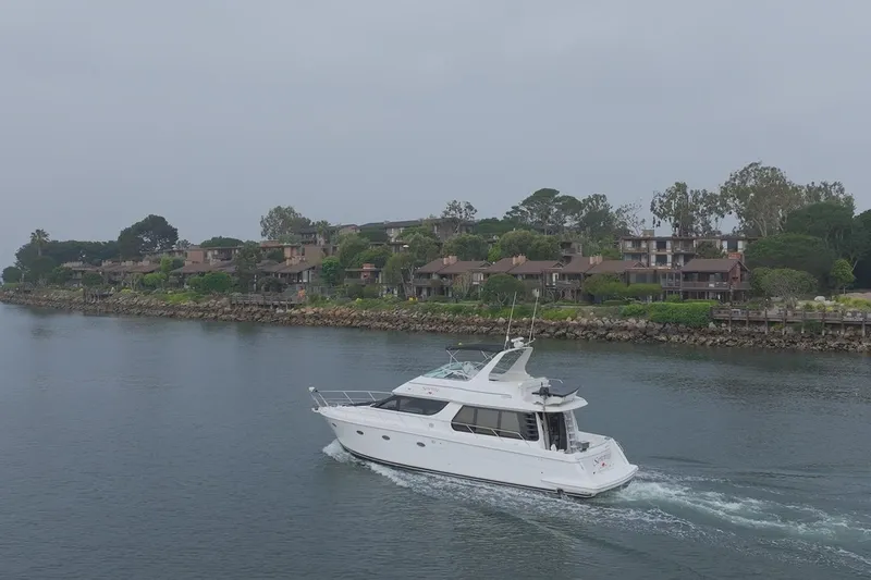 Slide: The Image of A 1999 Carver 53 Voyager yacht cruising near a scenic waterfront community. - 31