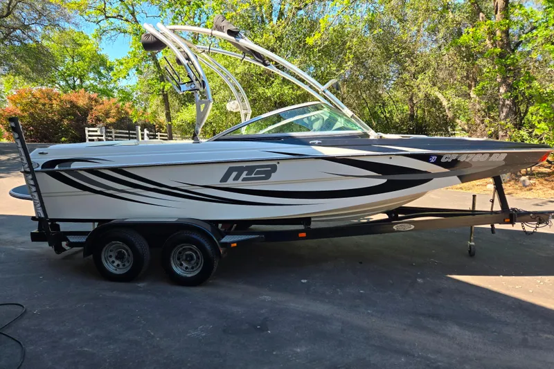 The Image of 2010 MB SPORTS 21 Tomcat boat on trailer, parked outdoors with trees in background. - 1
