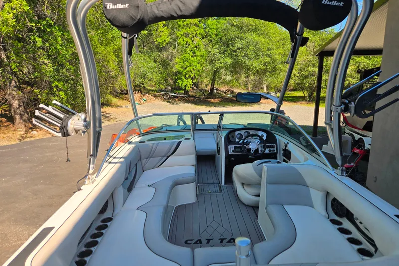 Slide: The Image of 2010 MB SPORTS 21 Tomcat boat interior with seating and steering wheel, surrounded by lush greenery. - 7