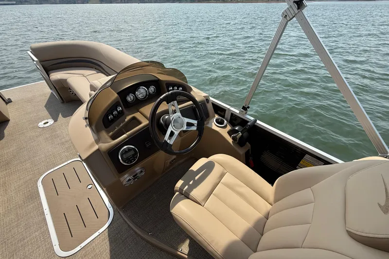 Slide: The Image of 2018 Bennington 23GSRFB boat interior with beige seating and steering wheel on a lake. - 11