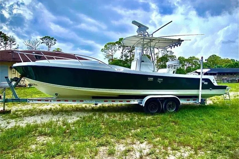 The Image of 2000 SeaVee 290B boat on trailer, parked on grassy area under cloudy sky. - 0