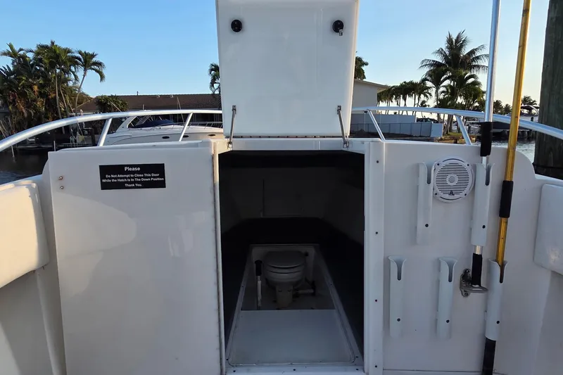 Slide: The Image of 2000 SeaVee 290B boat with open hatch revealing interior and toilet, docked near palm trees. - 26