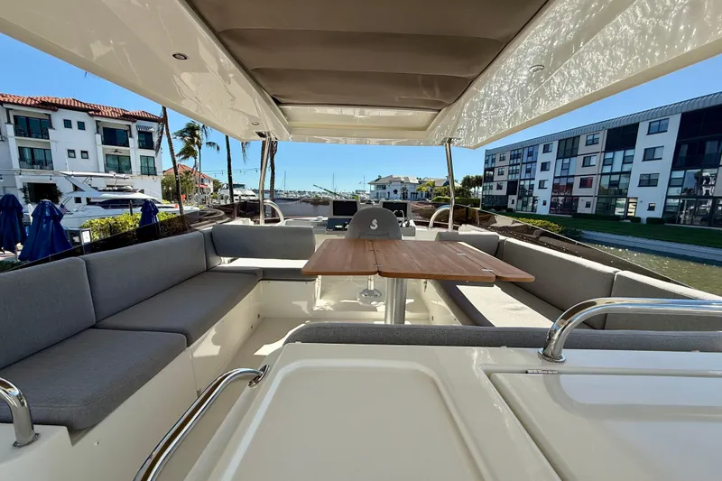 Slide: The Image of 2023 Beneteau Swift Trawler 48, spacious deck with seating and table, docked near modern buildings. - 11