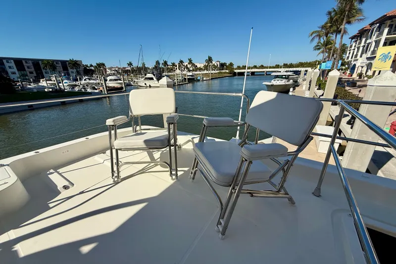 Slide: The Image of 2023 Beneteau Swift Trawler 48 deck with chairs, overlooking marina and palm trees. - 12