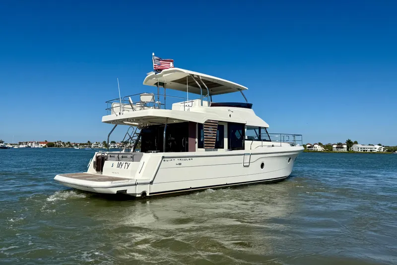 Slide: The Image of 2023 Beneteau Swift Trawler 48 cruising on a sunny day, with clear blue skies. - 2