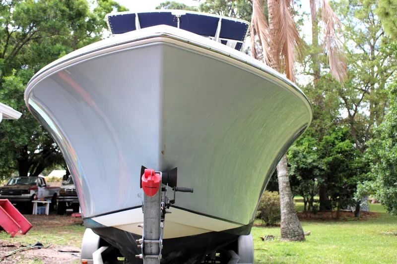 Slide: The Image of 2008 Sailfish 2660 CC boat on trailer, surrounded by lush greenery and parked vehicles. - 2