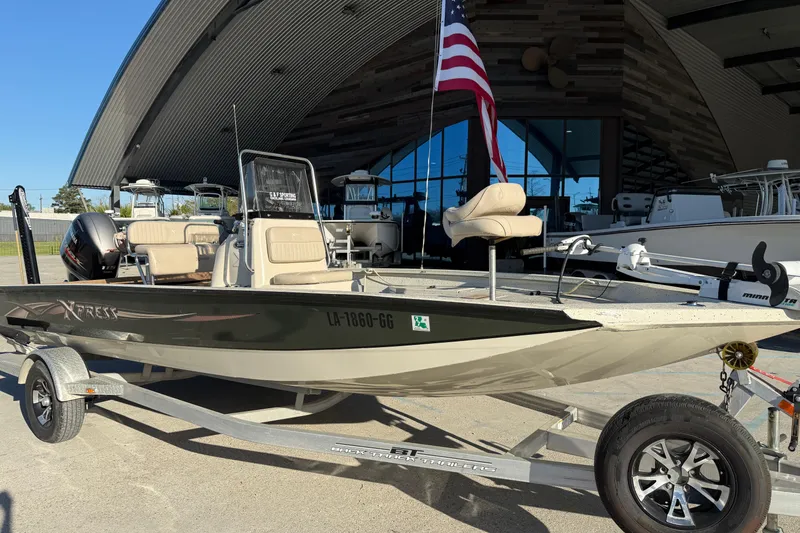 Slide: The Image of 2016 Xpress H20B Bay boat on trailer with American flag, parked outside a modern building. - 2