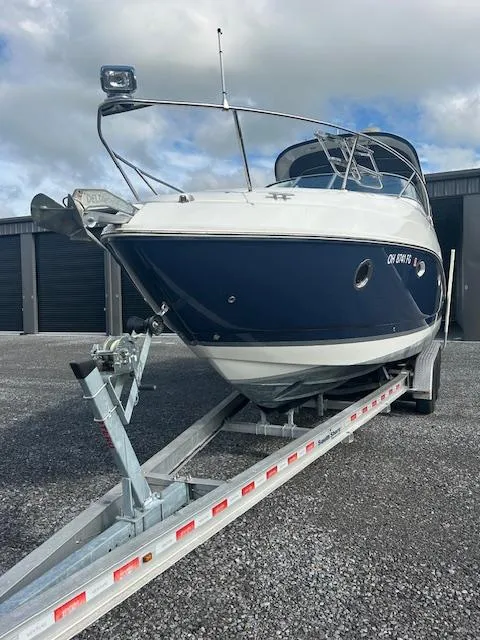Slide: The Image of 2013 Rinker 290 Express Cruiser on trailer, parked outdoors under cloudy sky. - 2