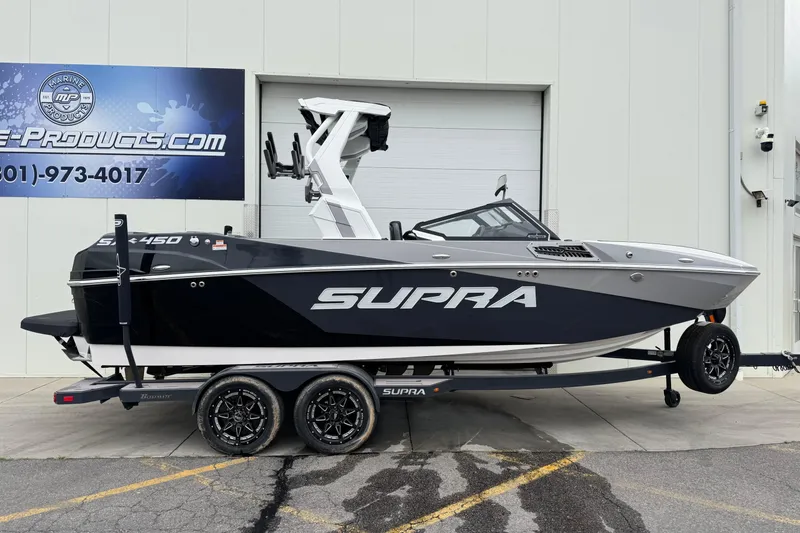 The Image of 2024 Supra SA 450 boat on trailer, parked outside a marine products store. - 0