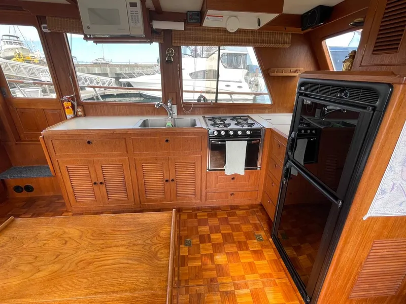 Slide: The Image of 1983 Ocean Alexander TRI Cabin kitchen with wooden cabinetry, stove, sink, and large windows. - 31