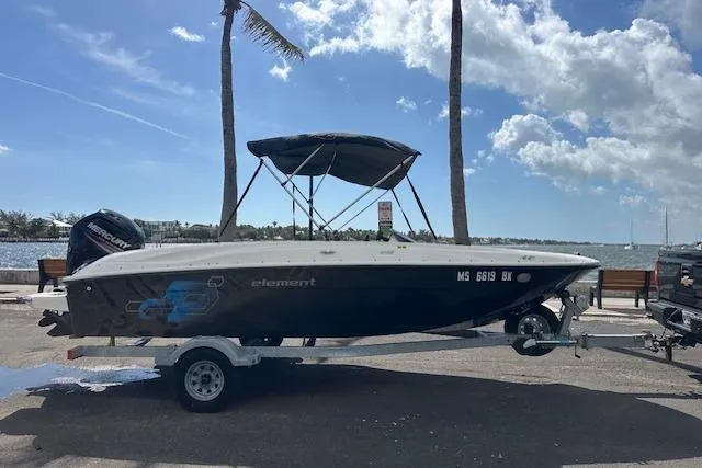 Slide: The Image of 2018 Bayliner Element E18 boat on trailer by waterfront, under clear blue sky. - 2