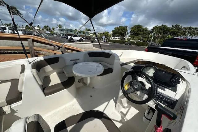 Slide: The Image of 2018 Bayliner Element E18 boat interior with seating, steering wheel, and table under canopy. - 8