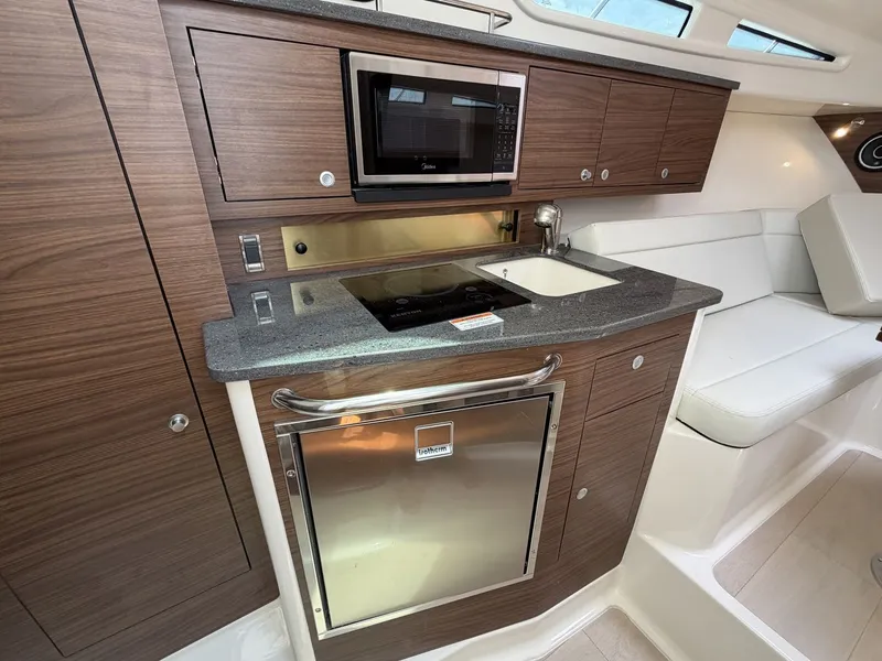 Slide: The Image of The 2027 Boston Whaler 325 Conquest galley features wood cabinets, a microwave, and a refrigerator. - 20