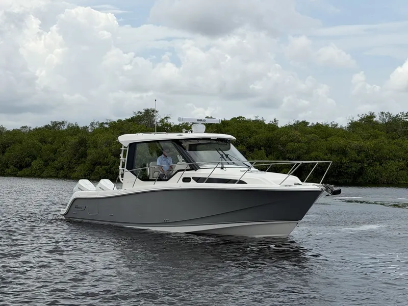 Slide: The Image of A 2027 Boston Whaler 325 Conquest cruising on calm waters, surrounded by lush greenery. - 1