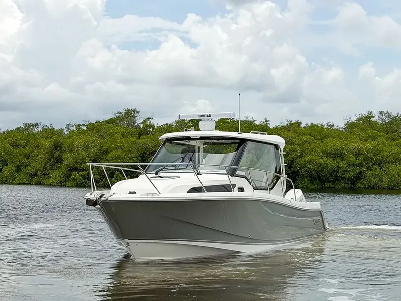 Slide: The Image of The 2027 Boston Whaler 325 Conquest cruises on calm waters, surrounded by lush greenery. - 29