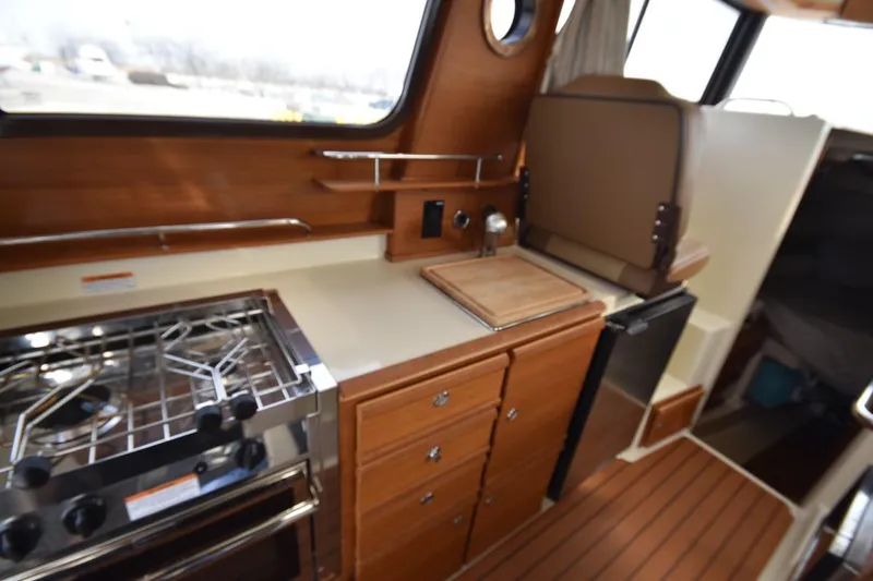 Slide: The Image of 2021 Ranger Tugs R-27 boat interior kitchen with stove, sink, and wooden cabinetry. - 27