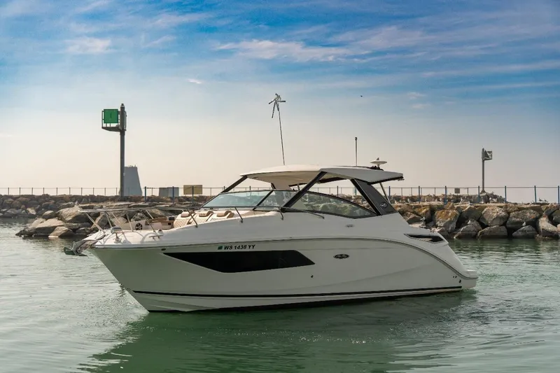 The Image of 2019 Sea Ray Sundancer 320 yacht cruising near rocky shoreline under clear sky. - 0