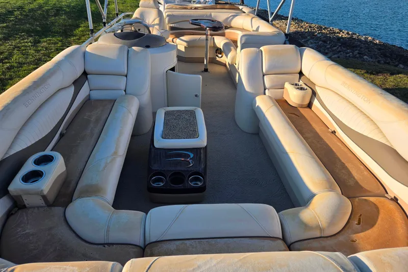 Slide: The Image of 2008 Bennington 2275RL pontoon boat interior with beige seating and cup holders by the water. - 10