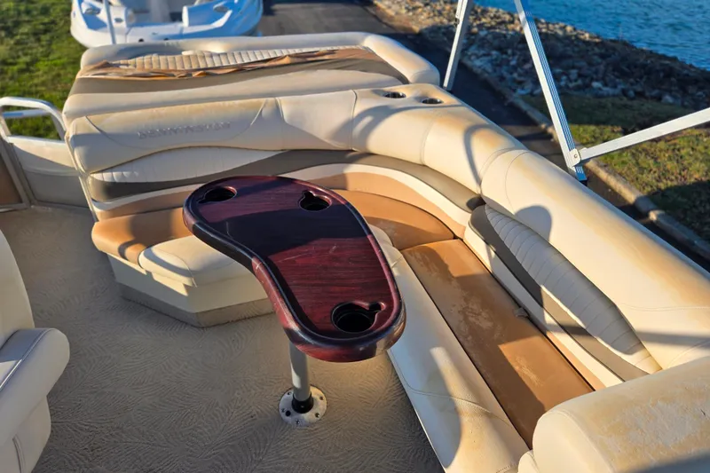 Slide: The Image of 2008 Bennington 2275RL boat interior with beige seating and wooden table by the water. - 16