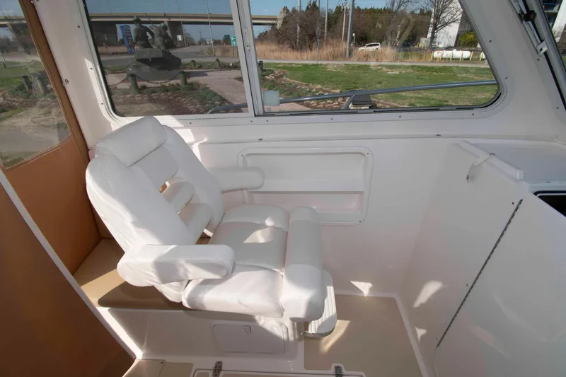 Slide: The Image of White captain's chair inside 2020 NorthCoast 235 HT boat, with large windows and outdoor view. - 12