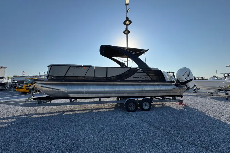 The Image of 2018 South Bay 725RS pontoon boat on trailer, parked outdoors under clear sky. - 1