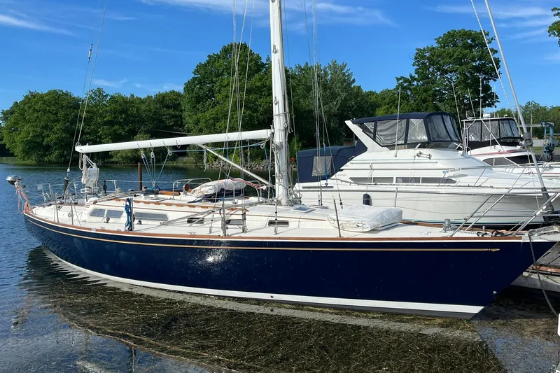 The Image of 1987 Sabre 42 sailboat docked on a calm lake with lush green trees. - 1