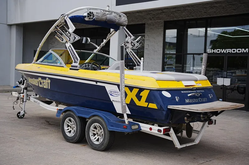 Slide: The Image of 2007 MasterCraft X10 boat on trailer outside showroom, featuring blue and yellow design. - 2