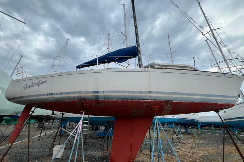 The Image of 1986 Alsberg Brothers Express 37 sailboat on stands, with blue and red hull, under cloudy sky. - 0