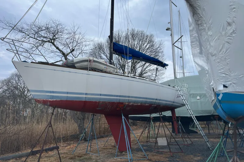 Slide: The Image of 1986 Alsberg Brothers Express 37 sailboat on stands, with blue and red hull, under cloudy sky. - 3