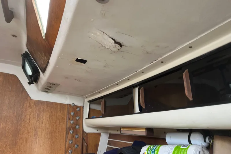 Slide: The Image of Interior of 1986 Alsberg Brothers Express 37 sailboat showing ceiling damage and storage area. - 54