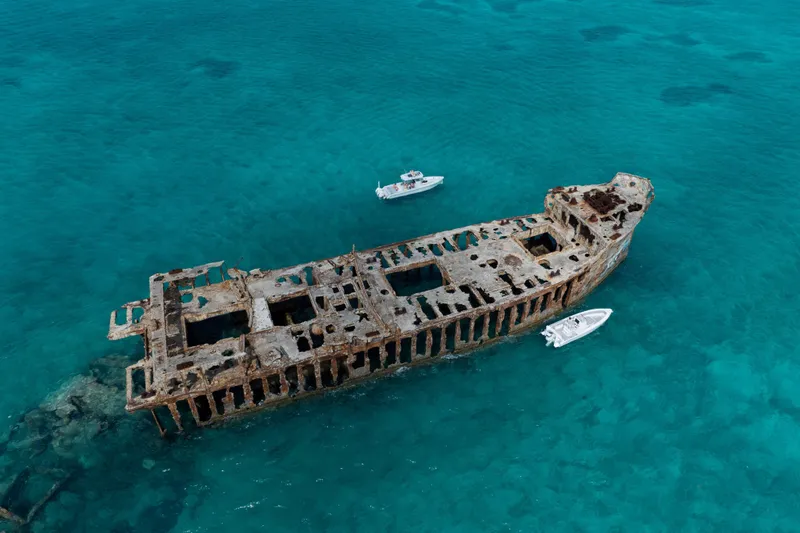Slide: The Image of Aerial view of a shipwreck surrounded by turquoise ocean waters, with two small boats nearby. - 13