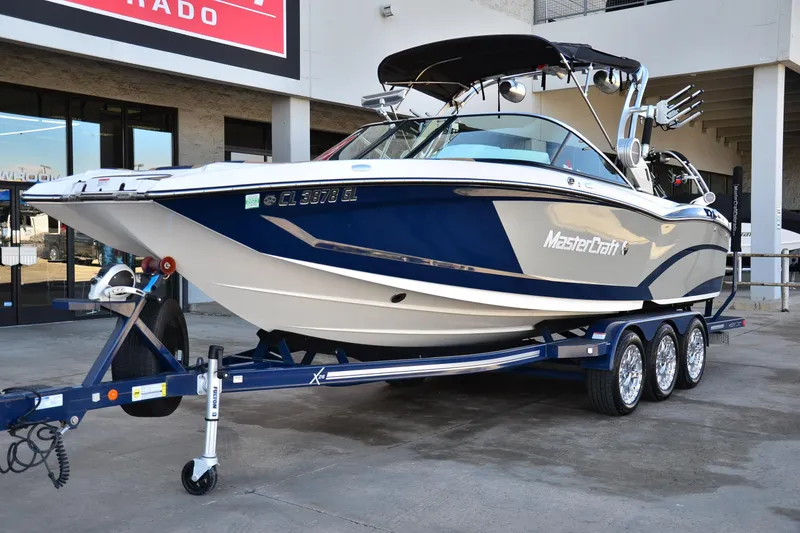 Slide: The Image of 2019 MasterCraft X26 boat on trailer, blue and white design, parked outside dealership. - 6