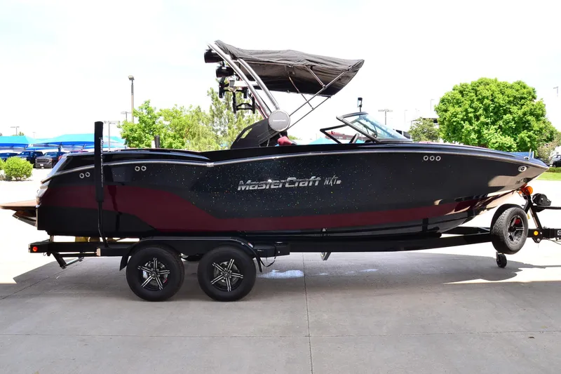 Slide: The Image of 2023 MasterCraft NXT23 boat on trailer, black and maroon design, parked outdoors. - 5