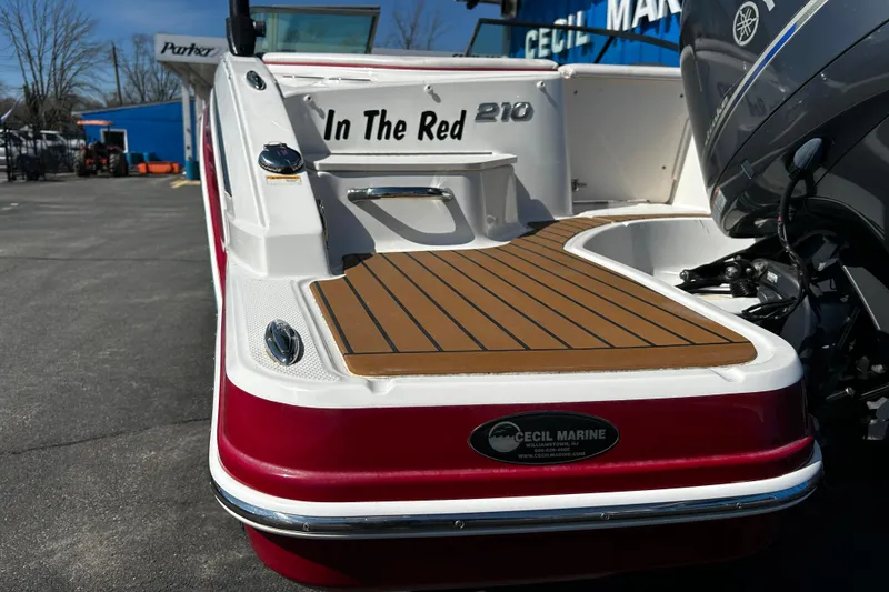 Slide: The Image of 2016 Chaparral 210 Suncoast boat with red exterior and teak deck, parked outdoors. - 30