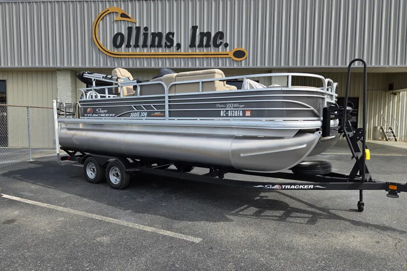 The Image of 2023 Sun Tracker Fishin' Barge 22 DLX pontoon boat on trailer outside dealership. - 0