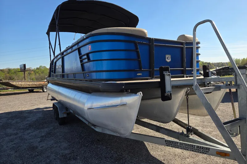 Slide: The Image of 2020 Godfrey AquaPatio 235 C pontoon boat on trailer, blue exterior, outdoor setting. - 2