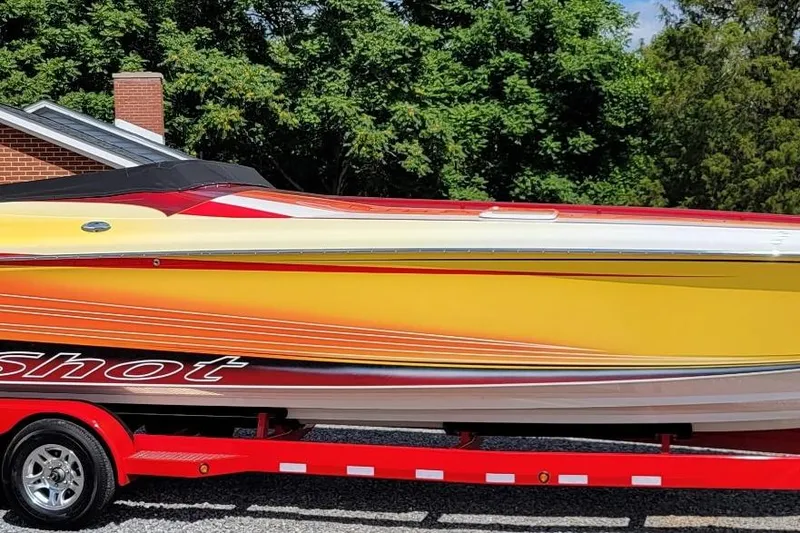 The Image of 2004 Hustler 388 SLINGSHOT speedboat with vibrant yellow and red design on a trailer. - 1