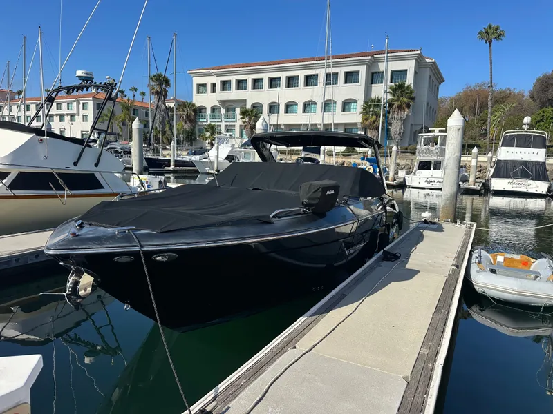 Slide: The Image of A sleek black motorboat docked at a marina, with buildings and palm trees in the background. - 27