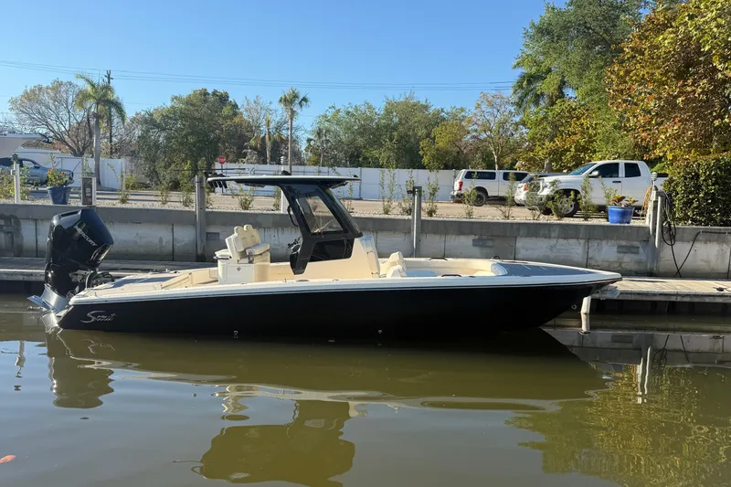 The Image of 2026 Scout 281 XSS boat docked on calm water, surrounded by trees and parked vehicles. - 0