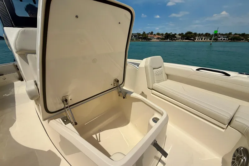 Slide: The Image of 2026 Scout 281 XSS boat interior with open storage compartment, beige seating, and ocean view. - 21