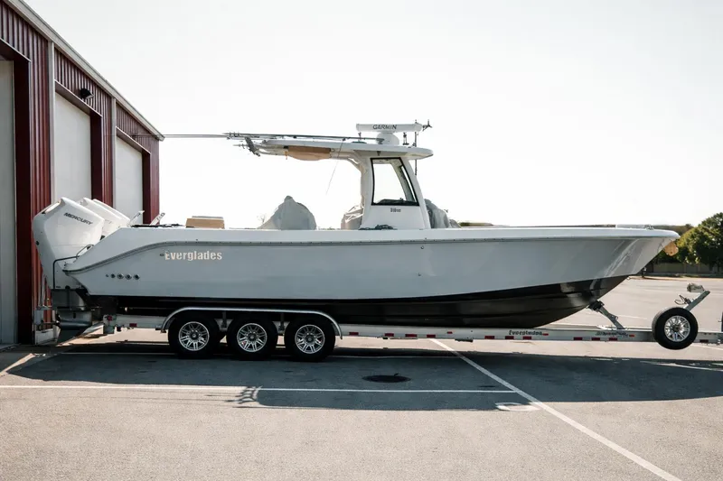 The Image of 2024 Everglades 315 Center Console boat on trailer, parked outside a building. - 0
