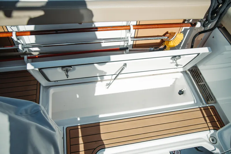 Slide: The Image of 2024 Everglades 315 Center Console boat storage compartment with wooden accents and cleaning tools. - 73