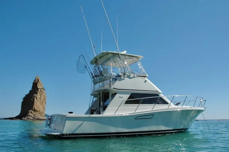 Slide: The Image of 2002 Skipjack 36 Flybridge yacht on clear blue water near a rocky outcrop. - 34