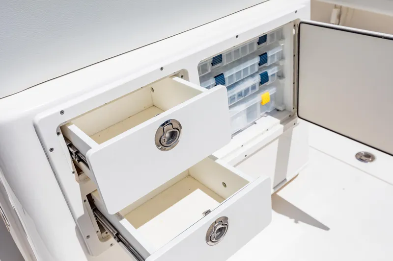 Slide: The Image of Storage compartments on a 2023 Cobia 240 Center Console boat, featuring drawers and tackle boxes. - 30