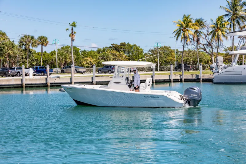 Slide: The Image of 2023 Cobia 240 Center Console boat cruising in a sunny marina with palm trees. - 8