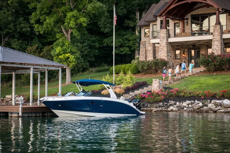 Slide: The Image of 2017 Sea Ray SDX 290 Outboard docked by a lakeside house with lush greenery. - 2