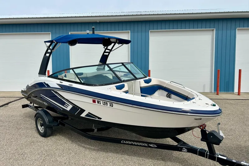 Slide: The Image of 2017 Chaparral 203 Vortex boat with blue accents on a trailer, parked near blue building. - 3